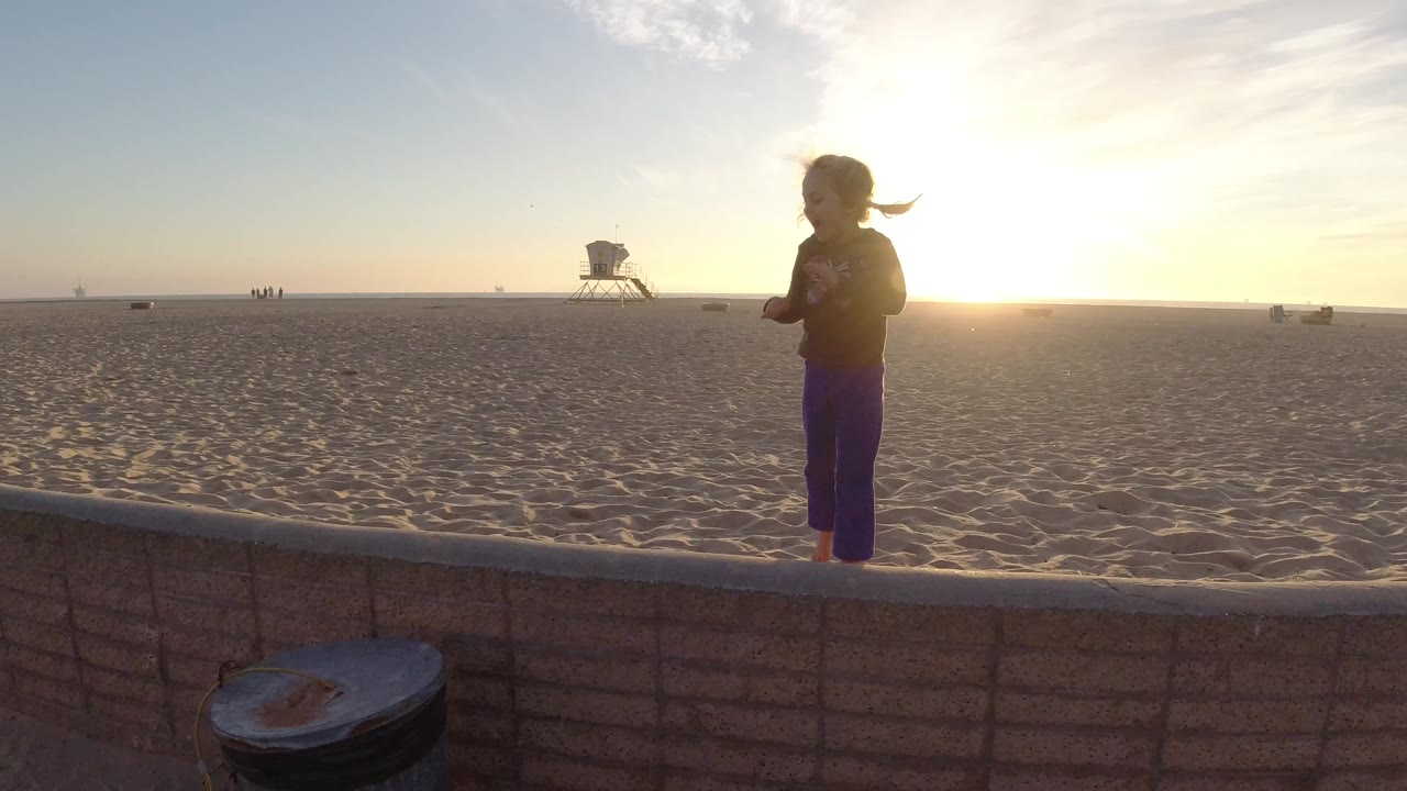 Young girl standing beside a low wall with a wide sandy beach behind her.