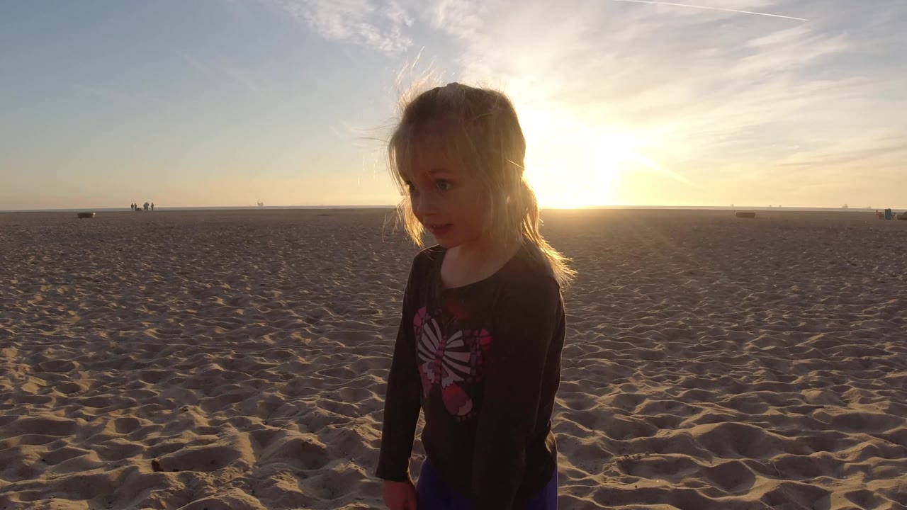 Child walking across beach sand with the sun behind their head.