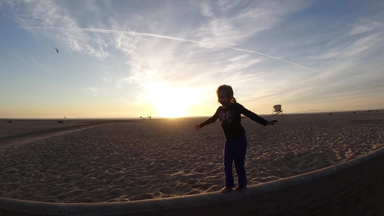 Child steps along beach edge with arms lowered
