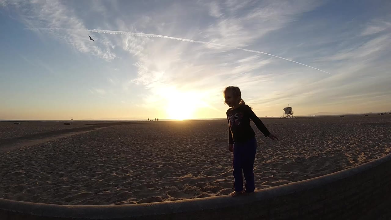 Backlit child standing on open beach sand.