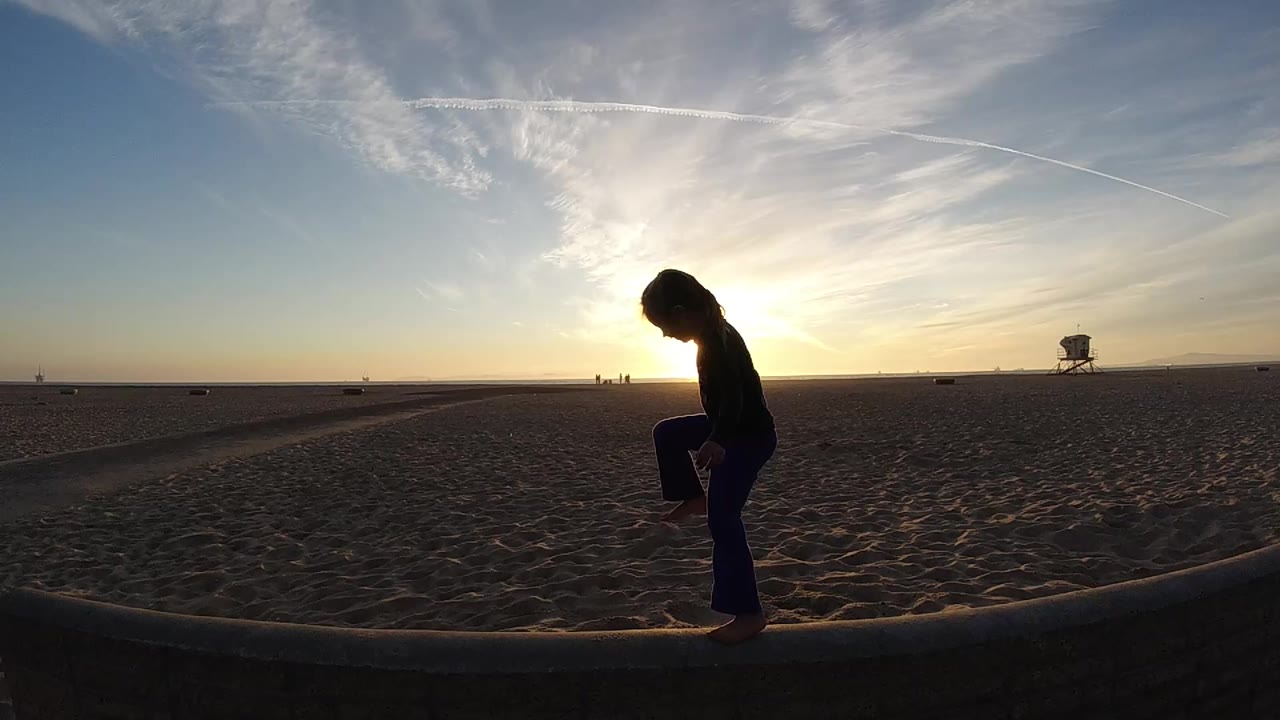 Silhouetted girl standing on the beach edge with one knee raised.