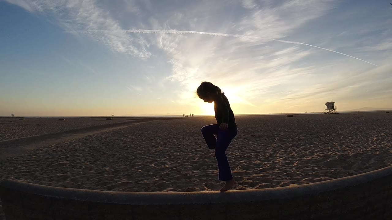 In Bolsa Chica, California, the silhouetted girl shifts slightly on the edge while the bright sun sits behind her and the lifeguard tower remains small on the right horizon.
