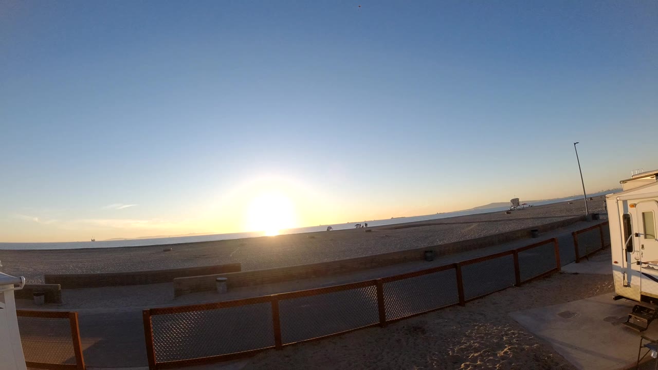 Bright sunrise above a quiet road and fenced foreground area.