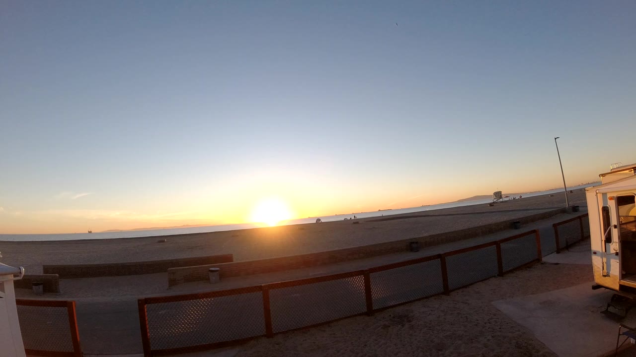 Bright sunrise over beach and path with a fence in the foreground.