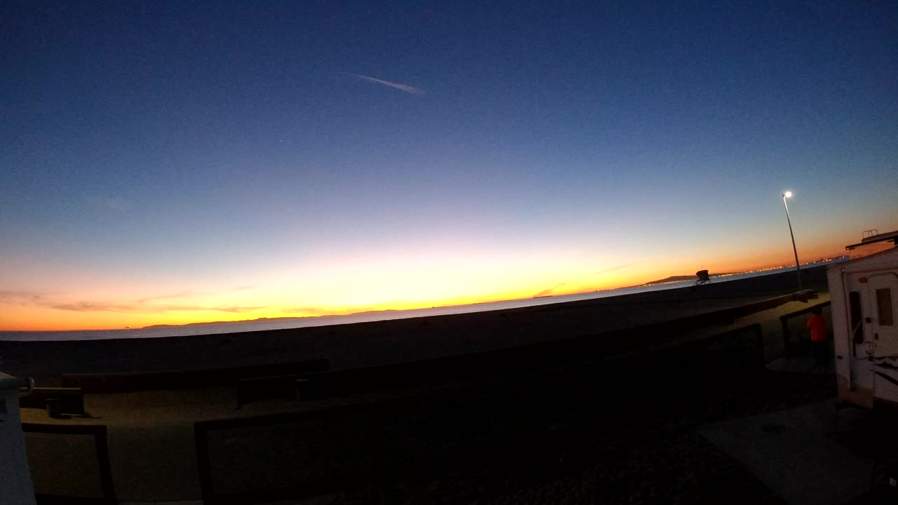 Bolsa Chica, California sunset horizon with orange light below a deep blue sky, a lit street light at right, dark foreground pavement, and no visible people.