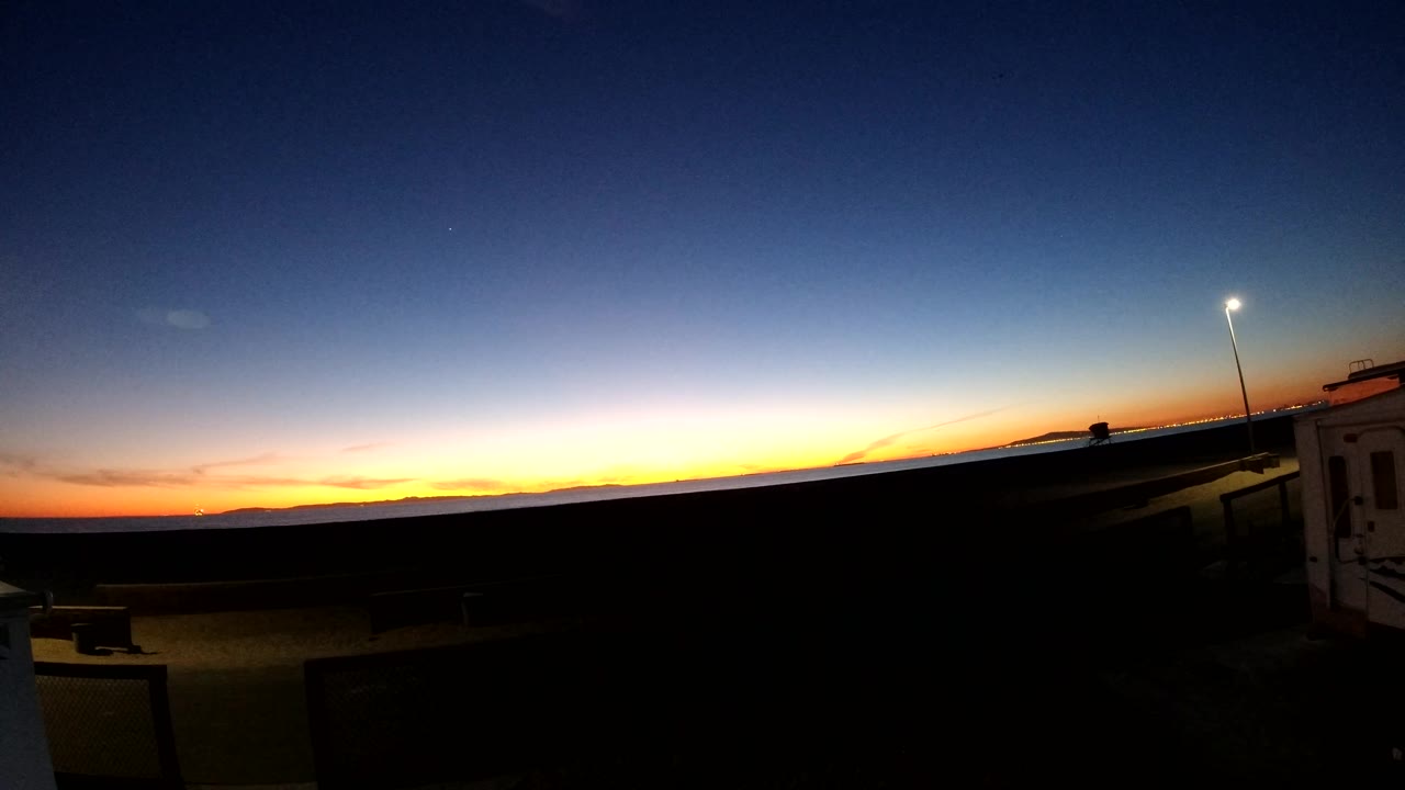 Street light over a dark road area with sunset color in the distance.