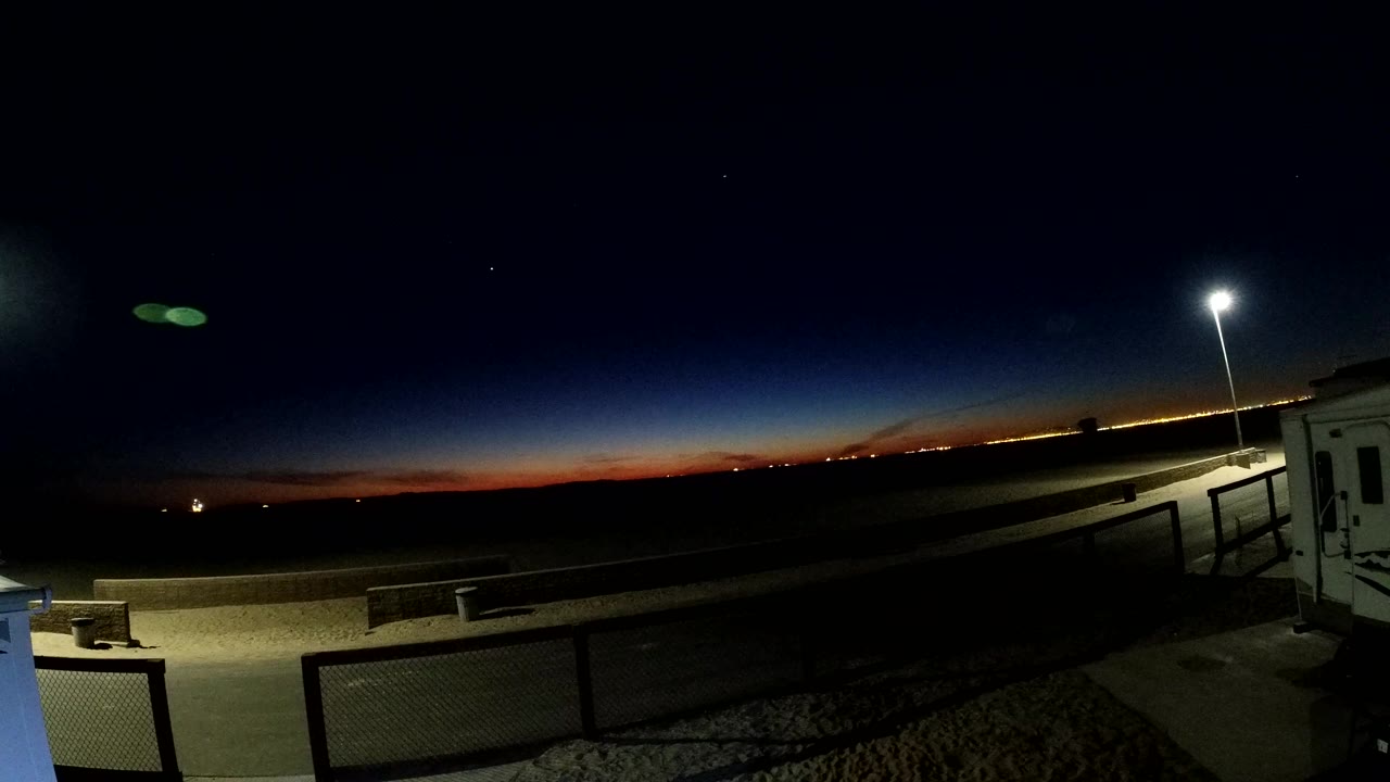 At Bolsa Chica, California, the third frame shows the sunset color narrowing along the horizon, distant lights appearing, a bright pole lamp, and no clearly visible people.