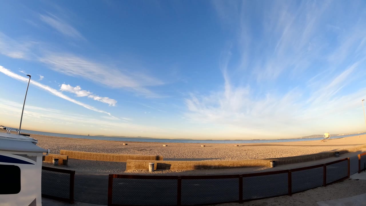 Opening frame of Bolsa Chica, California, showing a wide sandy shoreline, distant water, foreground railing, a road edge, and no visible people.