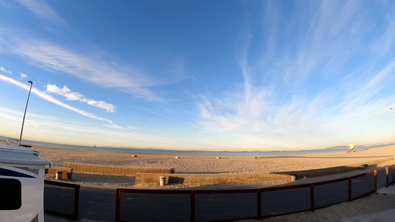 Bolsa Chica, California view with streaked high clouds, warm light on the sand, a straight distant horizon, foreground railing, and no visible people.