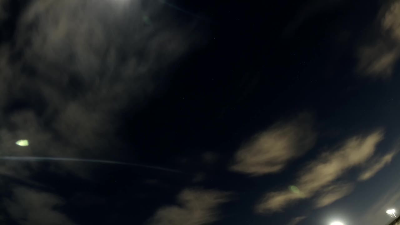 A bright round light hangs over soft, smeared clouds in the dark Bolsa Chica sky, with no visible people.