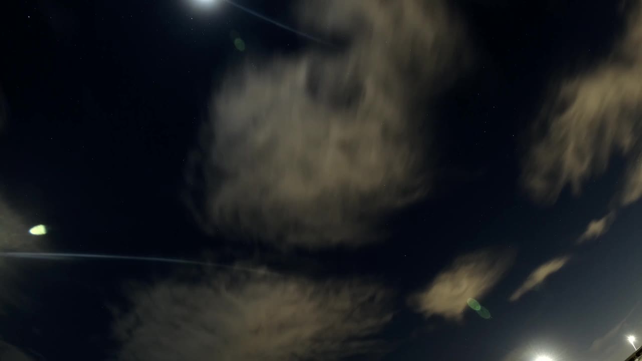Scattered tan cloud bands cross a blue-black Bolsa Chica sky while a bright light sits near the lower edge, with no visible people.