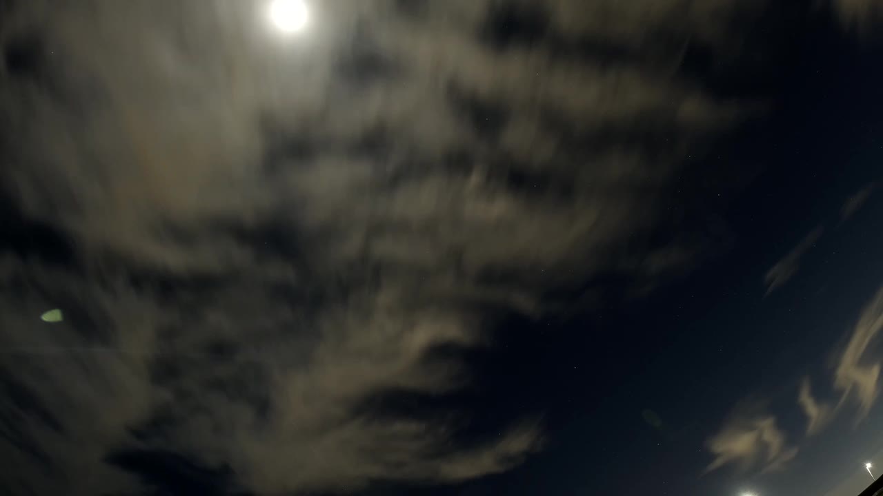 A large gray cloud mass fills the left side of the Bolsa Chica night sky while a bright white light glows near the top, with no visible people.