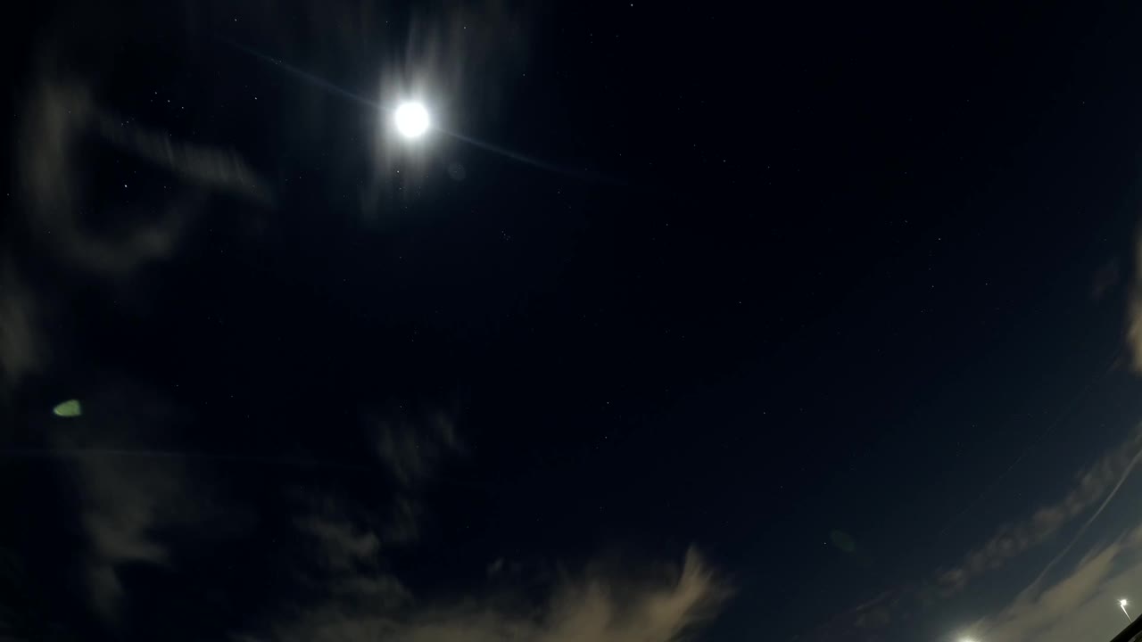 A bright sun sits near the top of a dark Bolsa Chica, California sky as wispy cloud streaks gather below, with no visible people.