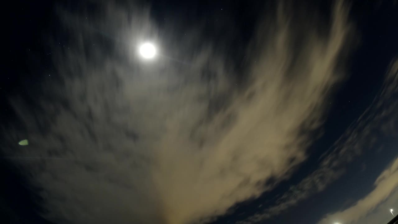A broad pale cloud mass moves across the dark Bolsa Chica, California sky near the bright sun, with no visible people.