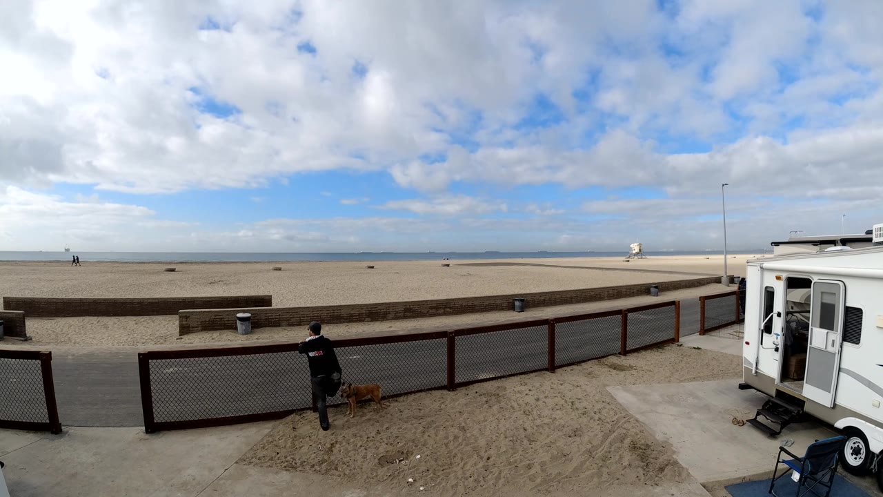 Person and dog near the left fence with the beach and trailer in view.