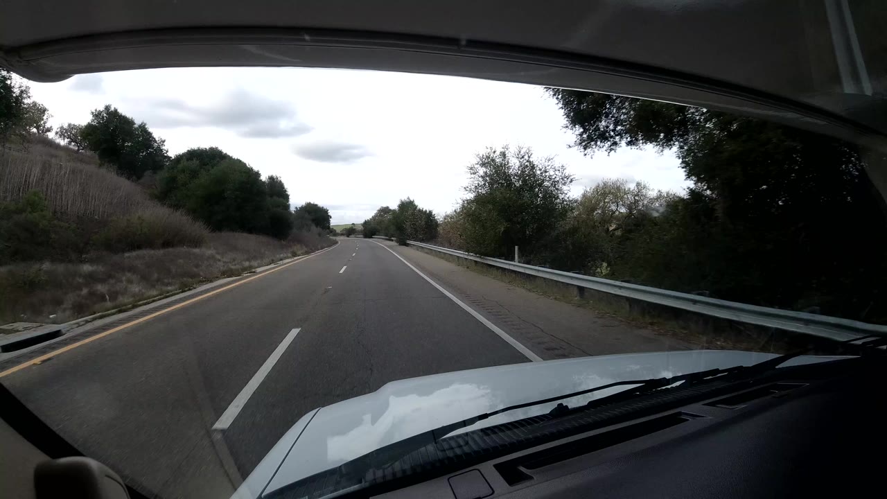 Highway curve with a guardrail and trees seen from inside a vehicle.