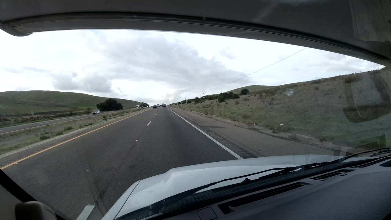 Forward highway view with traffic lanes, roadside grass, and cars in the distance.