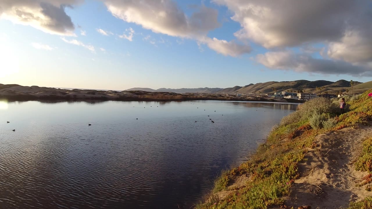 Water, hills, sandy path, scrub slope, and a small distant person near the right side.