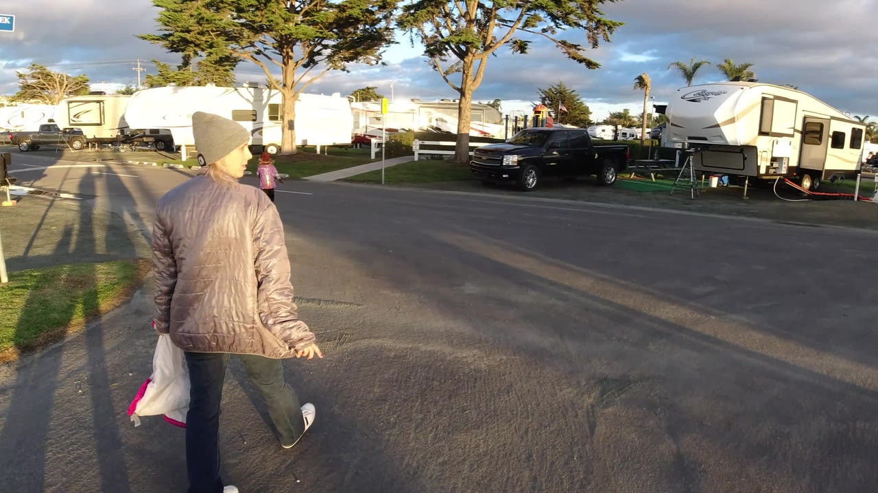 Walker crosses near the curb with RV trailers and a black truck across the street.