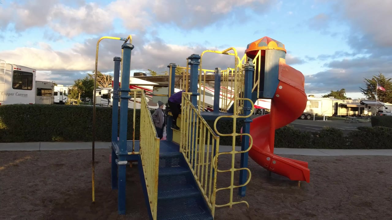 Playground platform, yellow railings, and orange slide with a child near the left side.