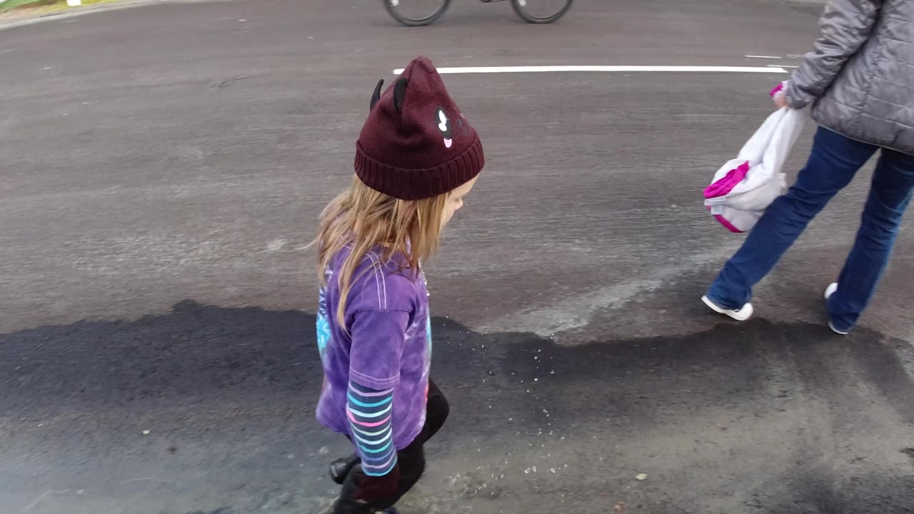 A child walks behind an adult carrying a white bag on a paved Pismo Beach street, with the adult partly cropped at the right edge.