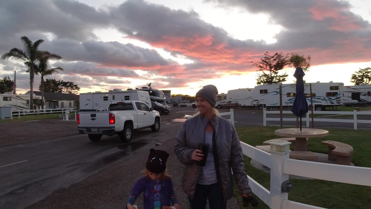 Woman smiling near child and dog as a pickup turns down an RV park road.