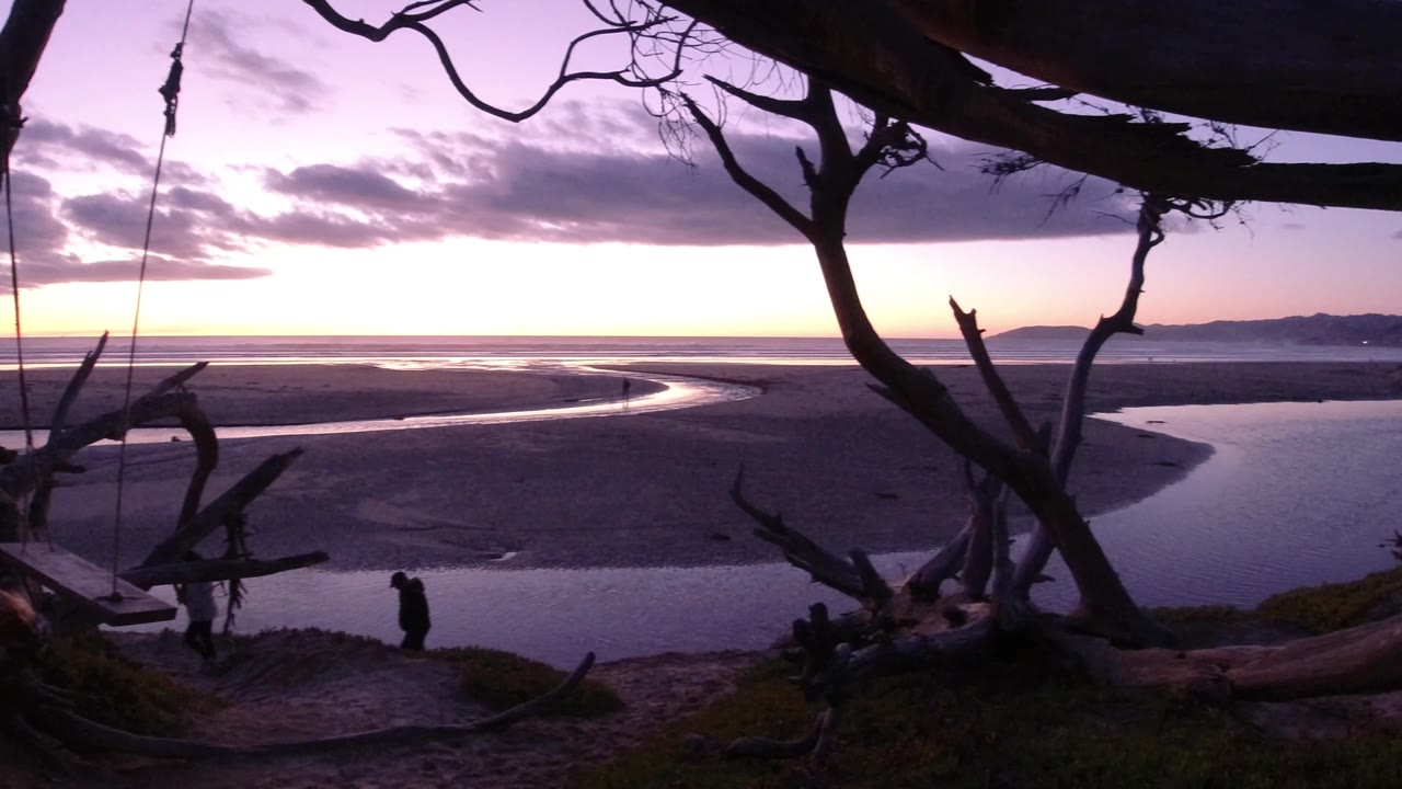 Purple morning sky over sand flats and curving water channel.