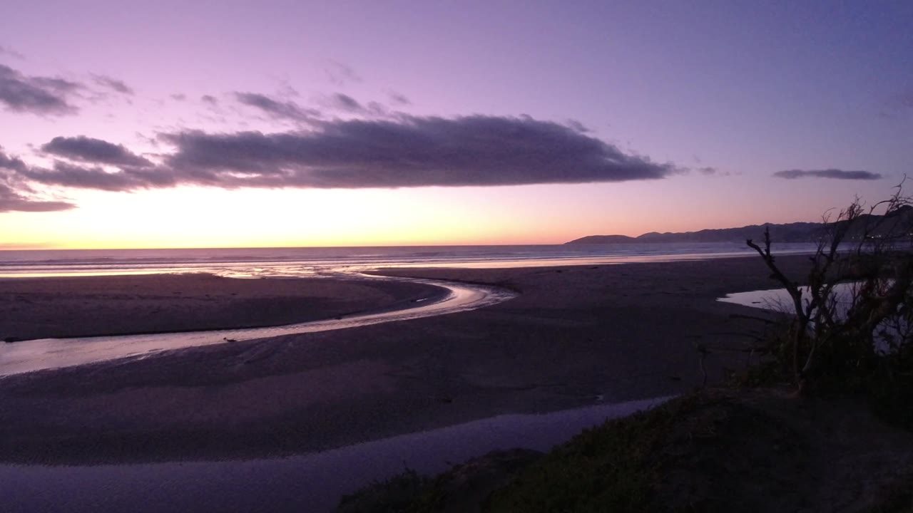 Twilight beach with curving tidal channel and dark clouds over the ocean.