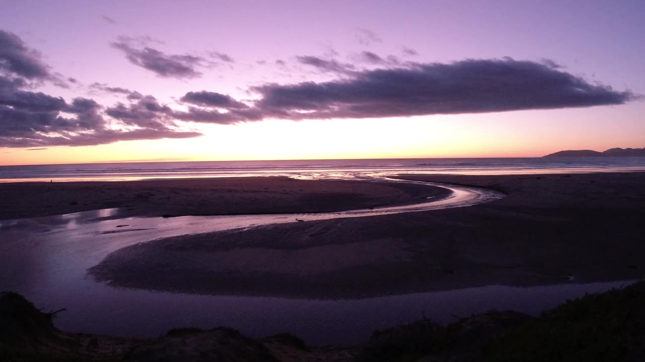 Pismo Beach, California sunset view over dark tidal flats, a curved reflective channel, low clouds, and no visible people at the start of the clip.