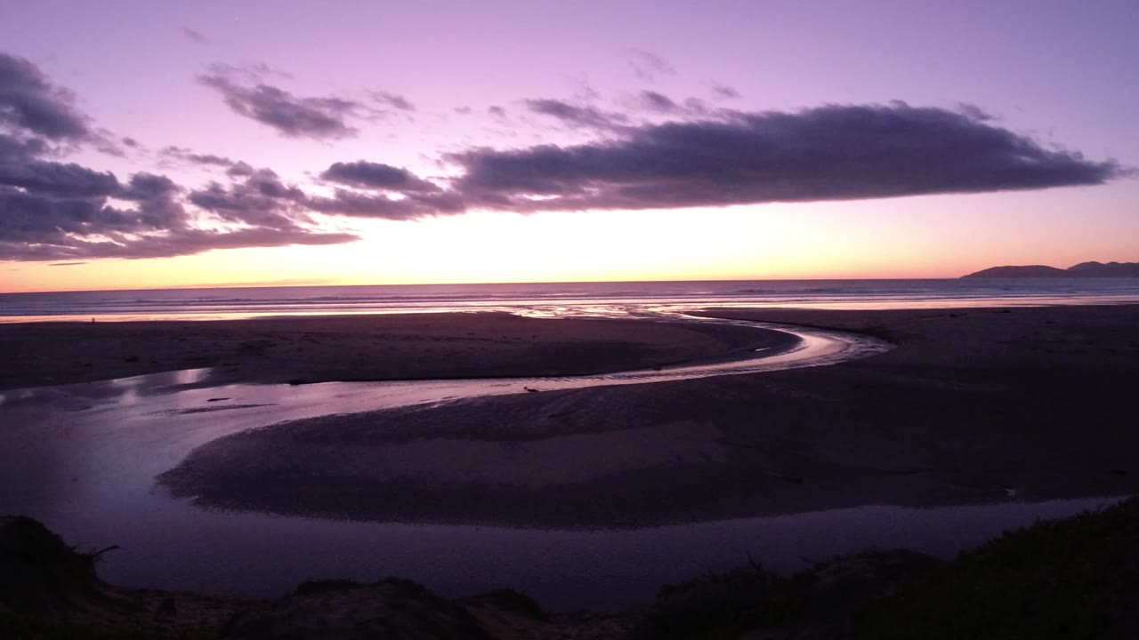 Dusk shoreline with low clouds above dark water and sandbars.