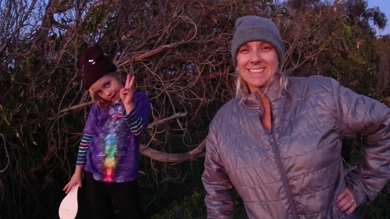 In Pismo Beach, the woman remains smiling at frame right while the girl stands at frame left with one hand raised and a white paddle partly visible.