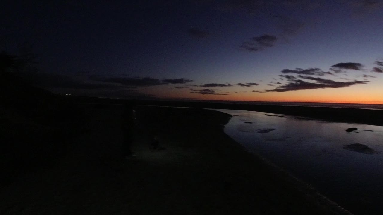 At 0:01, the elevated Pismo Beach view holds on dark water, a shadowed sand edge, and small clouds over the orange twilight strip, with no visible people.