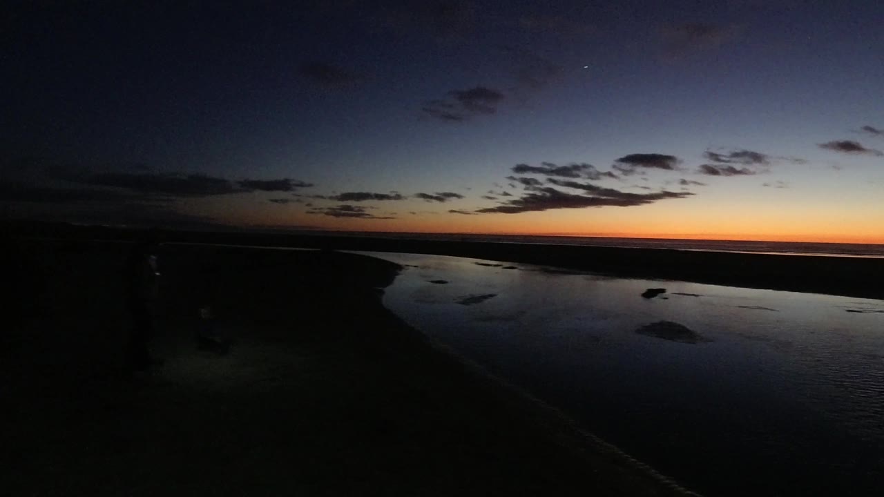 At 0:03, the view across Pismo Beach shows a curved dark waterline, shadowed beach, and layered dusk sky with orange near the horizon, with no visible people.
