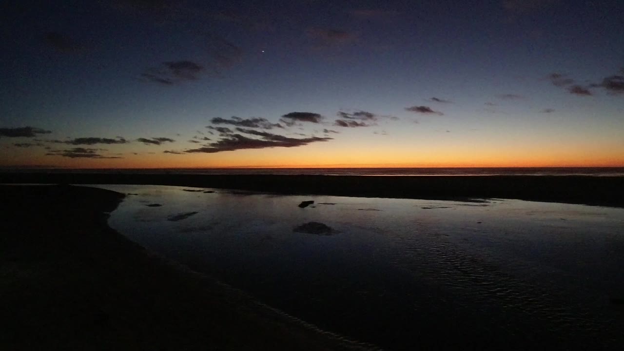 Dark coastal water below an orange sunset horizon and blue evening sky.
