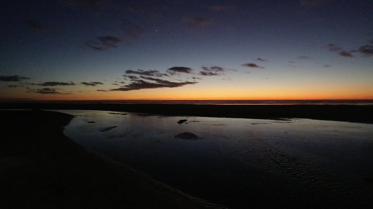 Pismo Beach, California twilight view with the waterline and dark shore slightly more centered beneath a blue sky and warm sunset band, with no visible people.