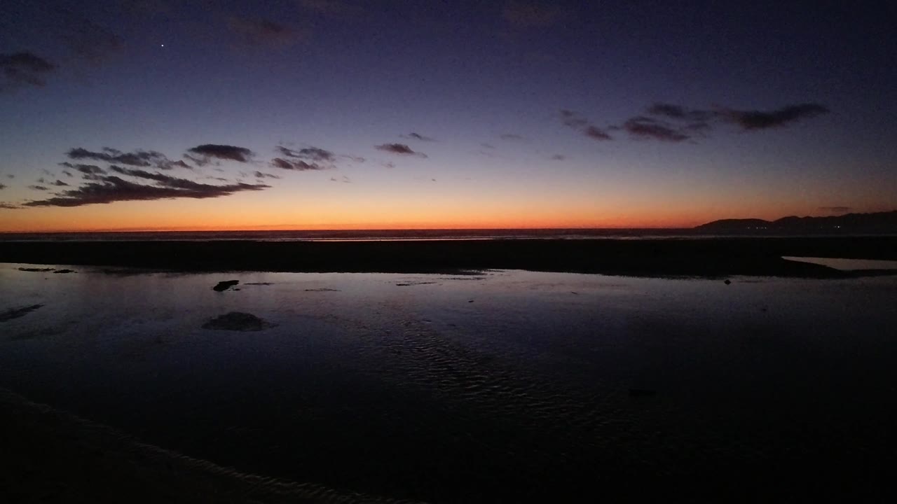 Dark clouds over orange sunset and reflective beach.