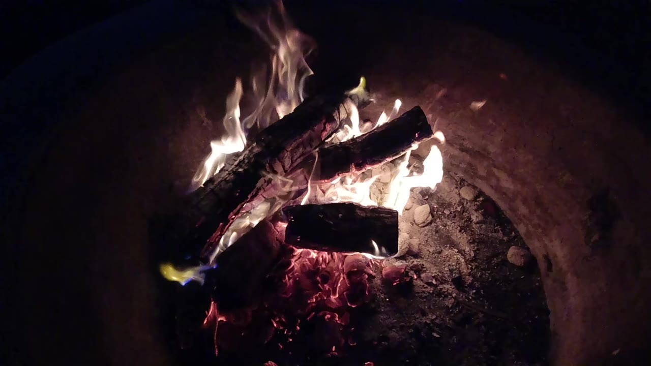 At 0:01, the same Pismo Beach fire pit shows flames wrapping higher around the upper log while red coals glow below, with no visible people.