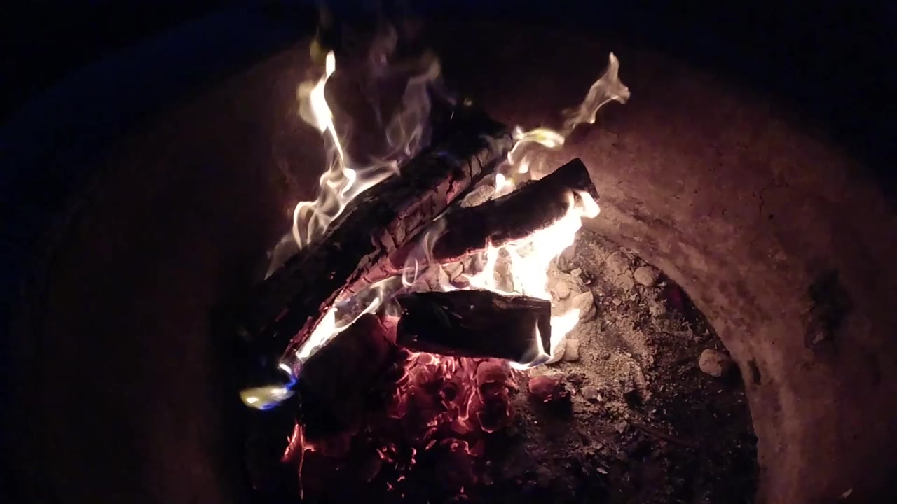 Pale flames curl higher around the stacked logs in the Pismo Beach fire pit, with red embers glowing below and no visible people.