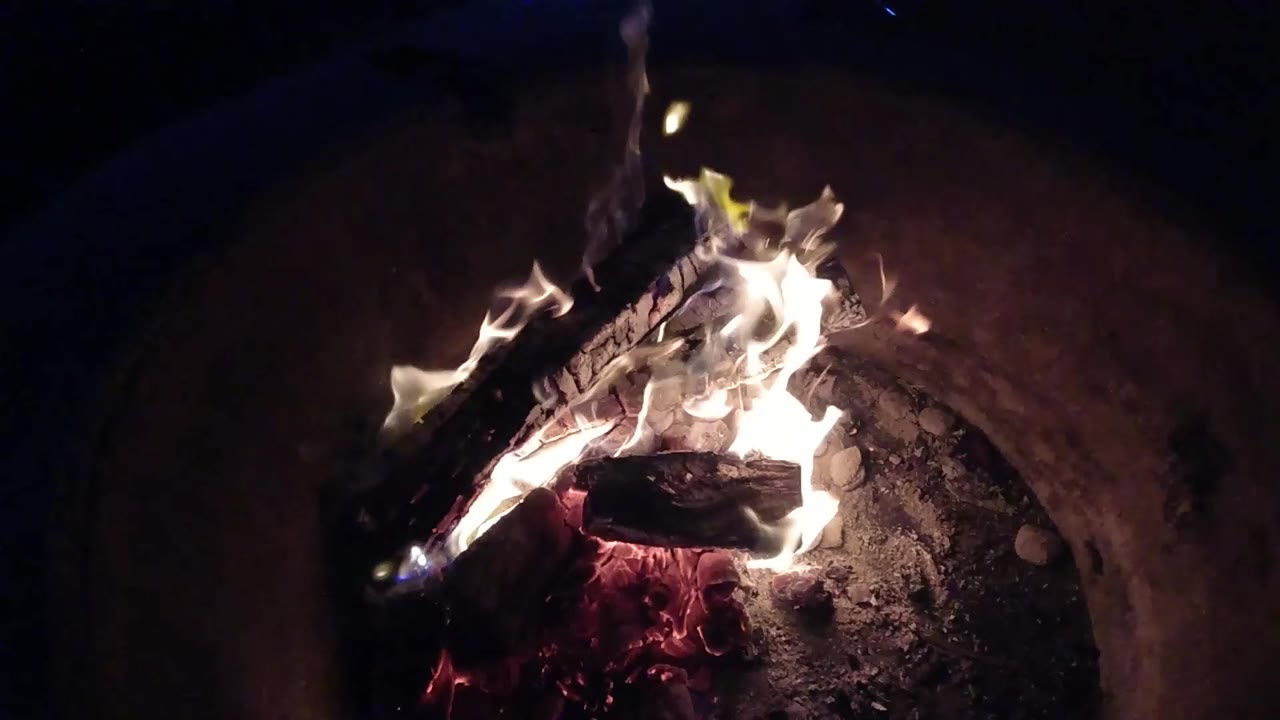 At 0:01, the flames spread higher around the stacked wood while the curved basin wall stays dim behind the fire in Pismo Beach, California, with no visible people.