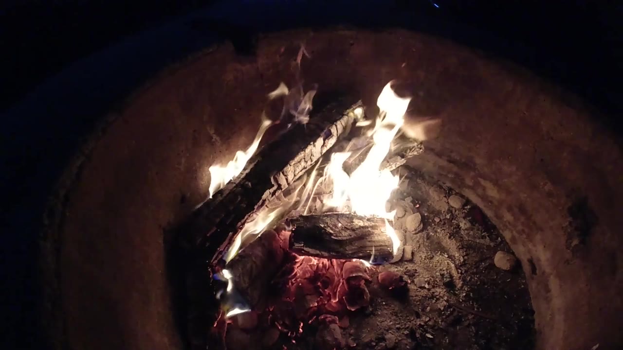 At 0:02, the flames lean across the upper log while the fire pit rim stays mostly dark around the Pismo Beach, California fire detail, with no visible people.
