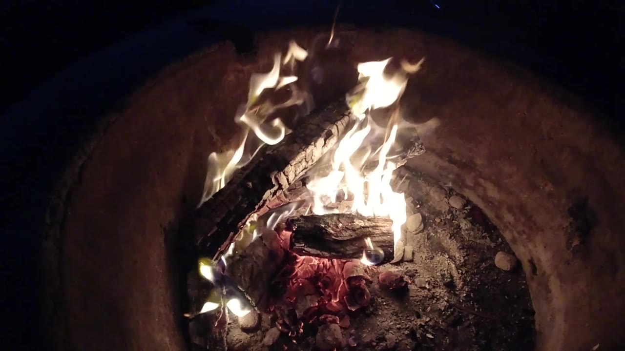 Bright flames flaring over logs with ash and embers below.