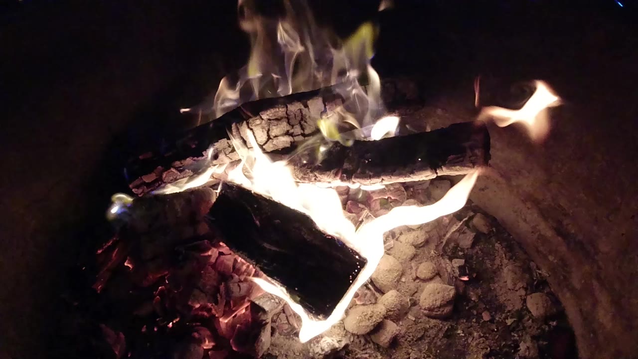 Burning logs and bright flames inside a metal barrel.