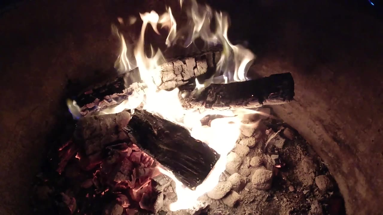 At 0:02, the fire flares brighter across stacked charred wood inside the metal barrel in Pismo Beach, California, with no visible people.