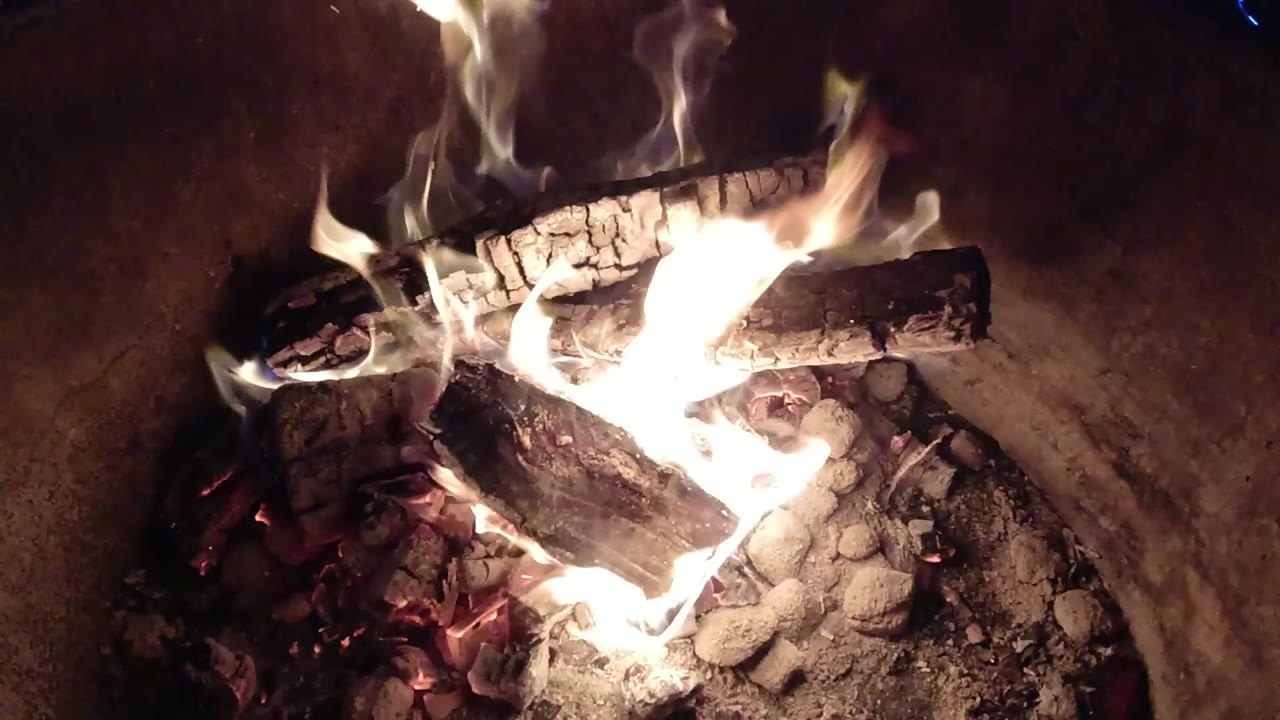 Charred firewood glowing as flames rise around the logs.