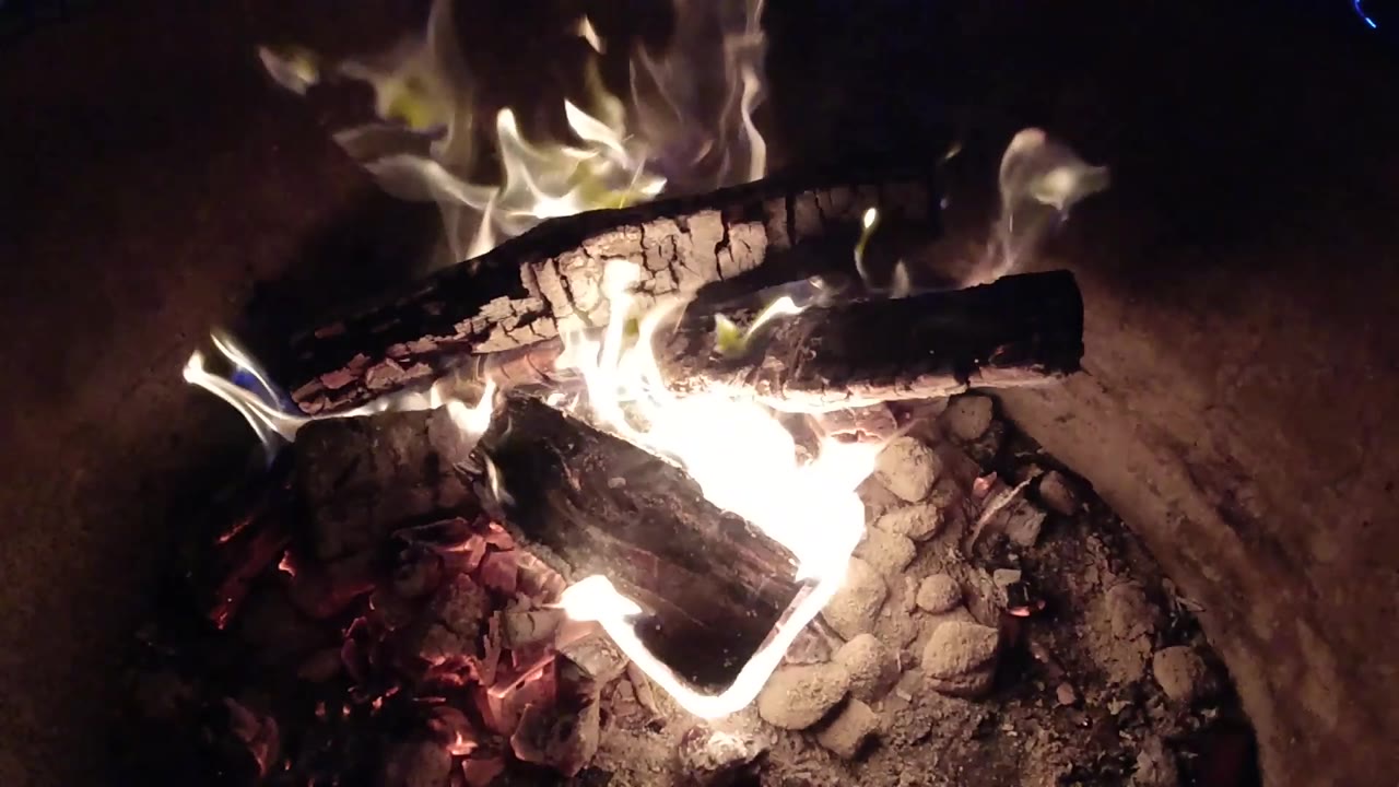 The fire pit remains tightly framed as a front log catches bright flame beneath two darker upper logs in Pismo Beach, with no visible people.