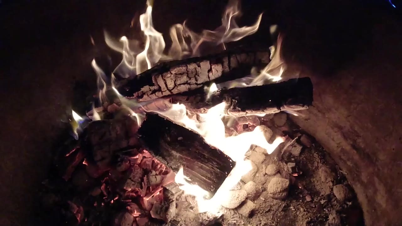 Charred logs burning over coals in a dark fire pit.