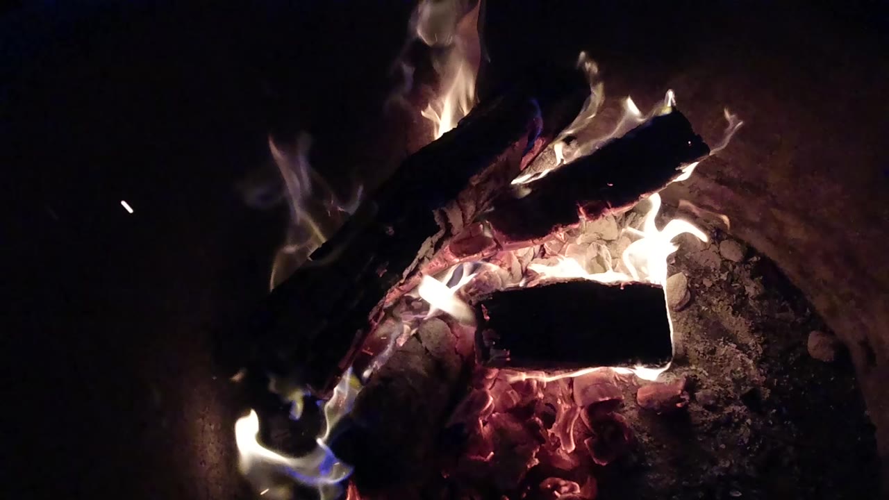 Burning logs in a dark fire pit at night.