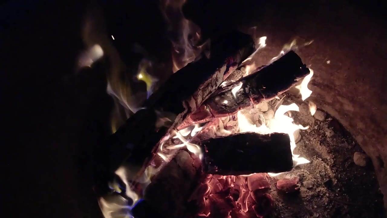 At 0:03, pale flames curl upward from the left and center of the Pismo Beach fire pit while red embers glow below, with no visible people.