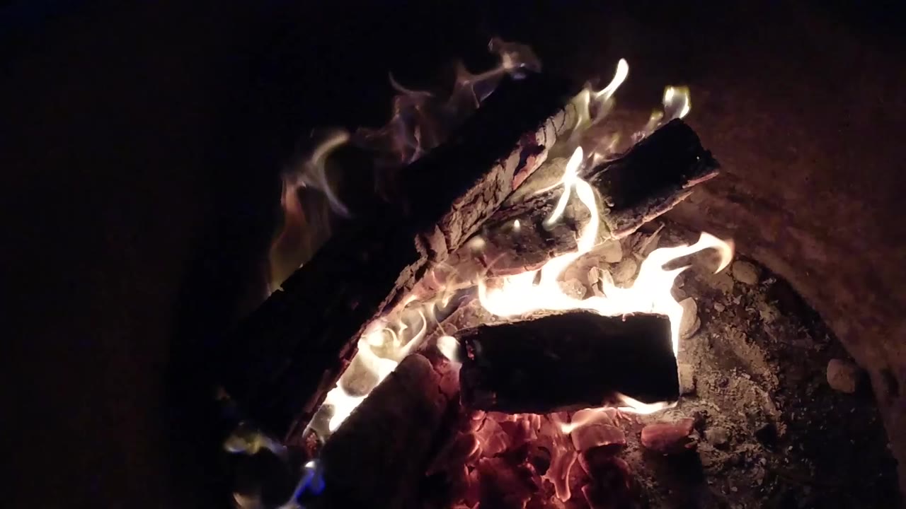 Three burning logs in a fire pit with embers and flames.