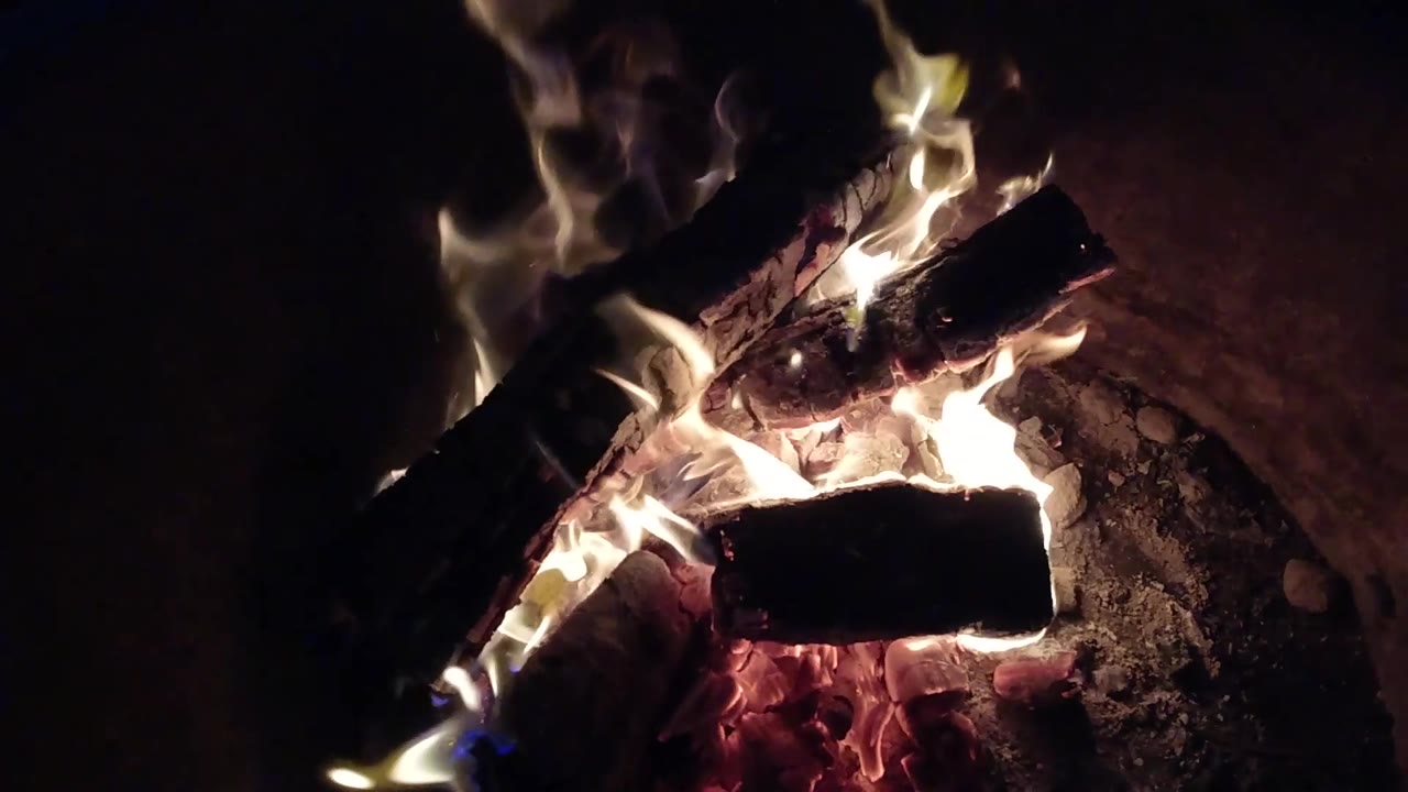 Taller flames lift from the left and upper logs in the Pismo Beach fire pit, with glowing coals below and no visible people.